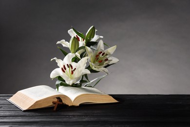 Bible, cross and lilies on dark wooden table against gray background, space for text. Religion of Christianity