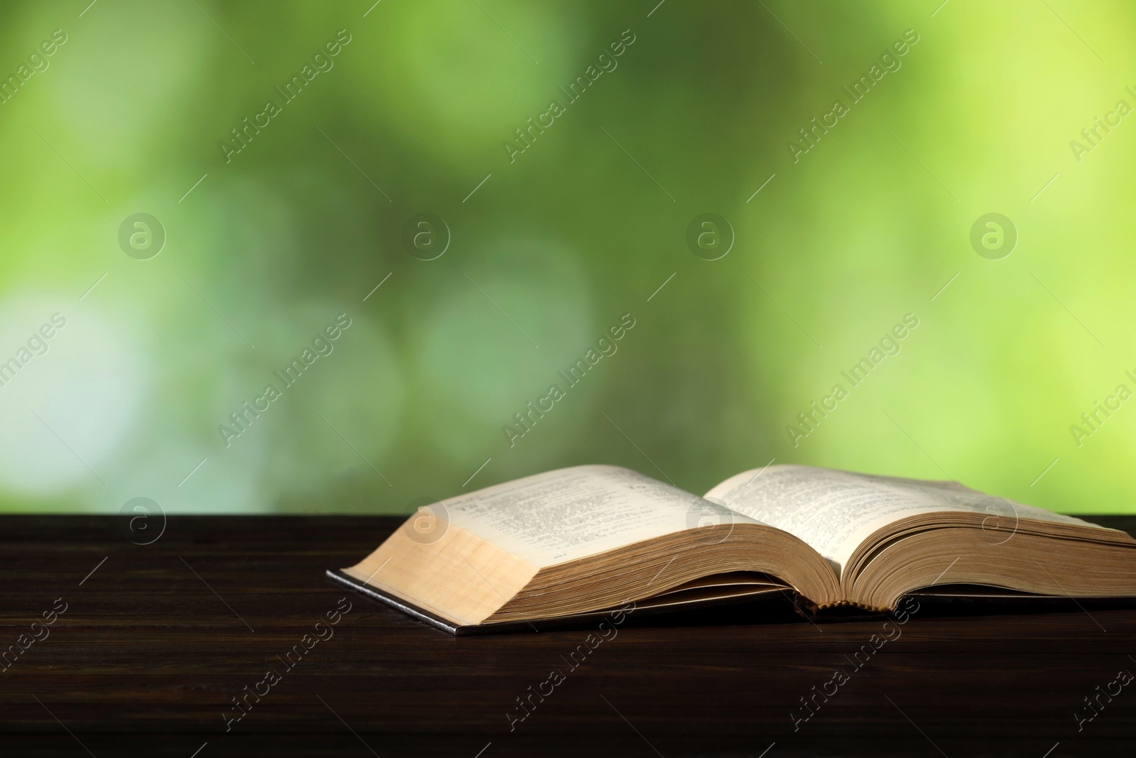 Photo of Bible on wooden table against blurred green background, space for text. Religion of Christianity