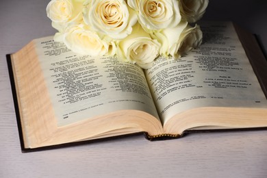 Bible and roses on light wooden table, closeup. Religion of Christianity