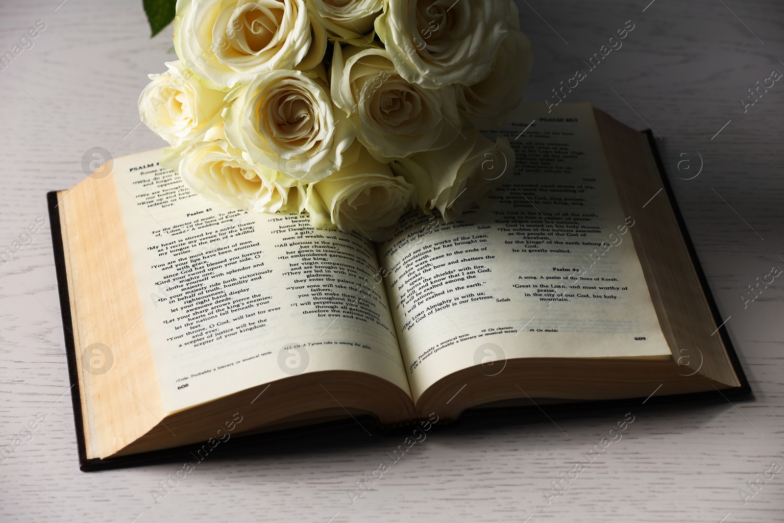 Photo of Bible and roses on light wooden table, closeup. Religion of Christianity