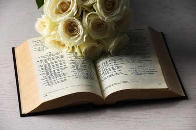 Bible and roses on light wooden table, closeup. Religion of Christianity