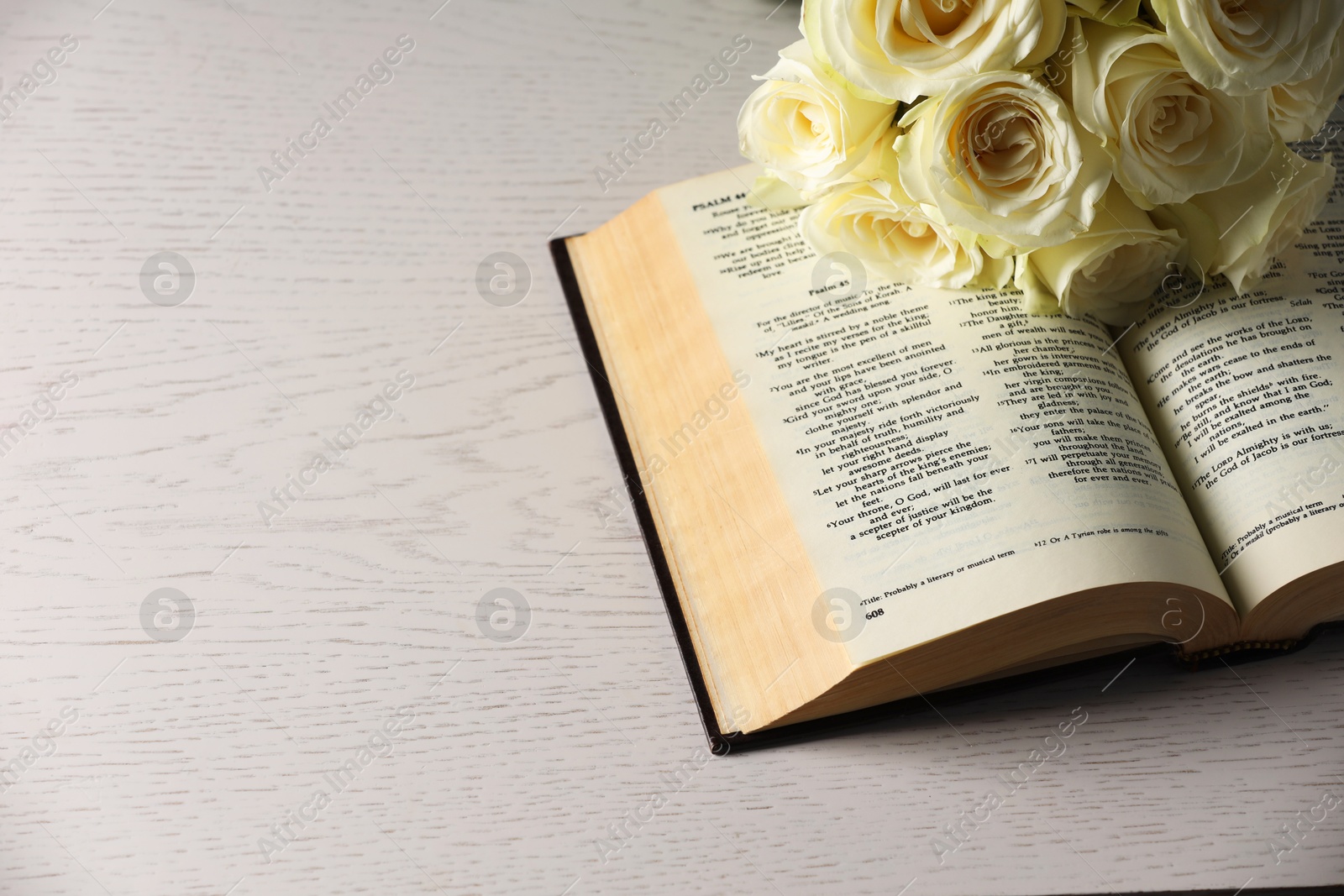 Photo of Bible and roses on light wooden table, space for text. Religion of Christianity