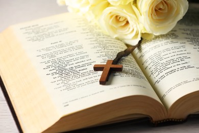 Photo of Bible, cross and roses on light table, closeup. Religion of Christianity