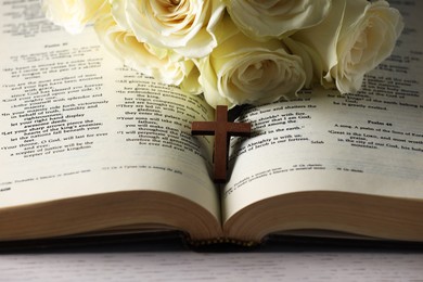 Bible, cross and roses on light table, closeup. Religion of Christianity