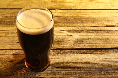 Glass of beer with froth on wooden table, space for text