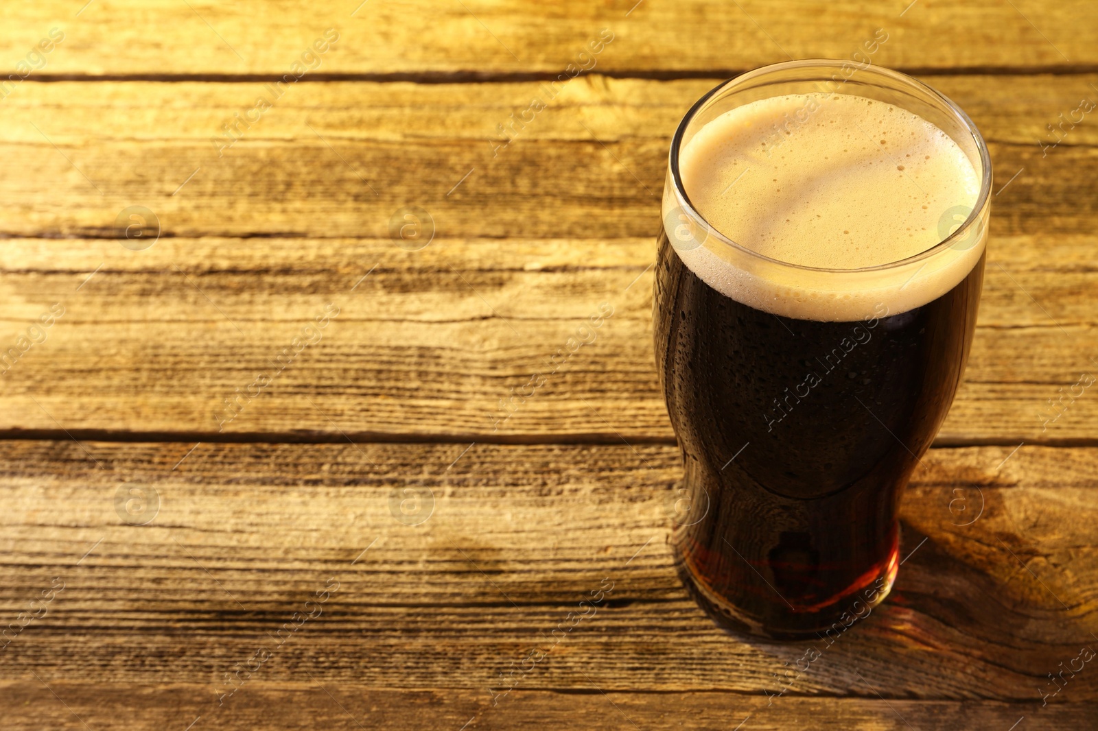 Photo of Glass of beer with froth on wooden table, space for text