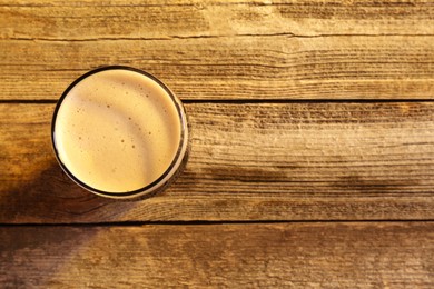 Photo of Glass of beer with froth on wooden table, top view. Space for text