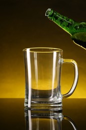 Pouring beer into glass mug from bottle on dark table, closeup