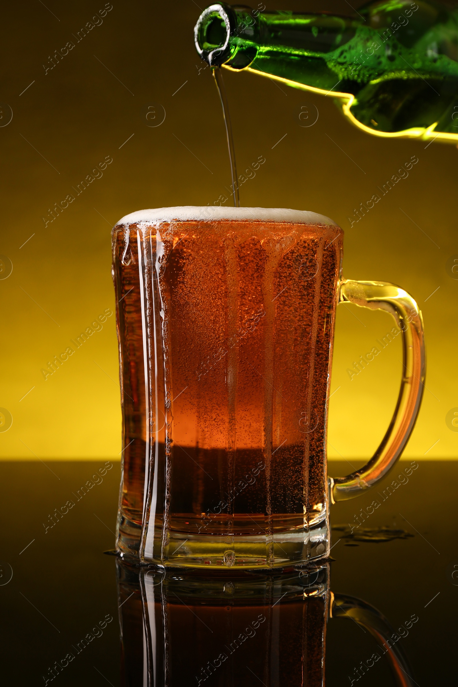 Photo of Pouring beer into glass mug from bottle on dark table, closeup