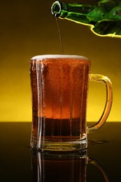 Photo of Pouring beer into glass mug from bottle on dark table, closeup