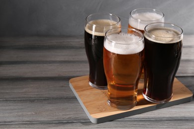 Photo of Glasses with different types of beer on grey wooden table, space for text