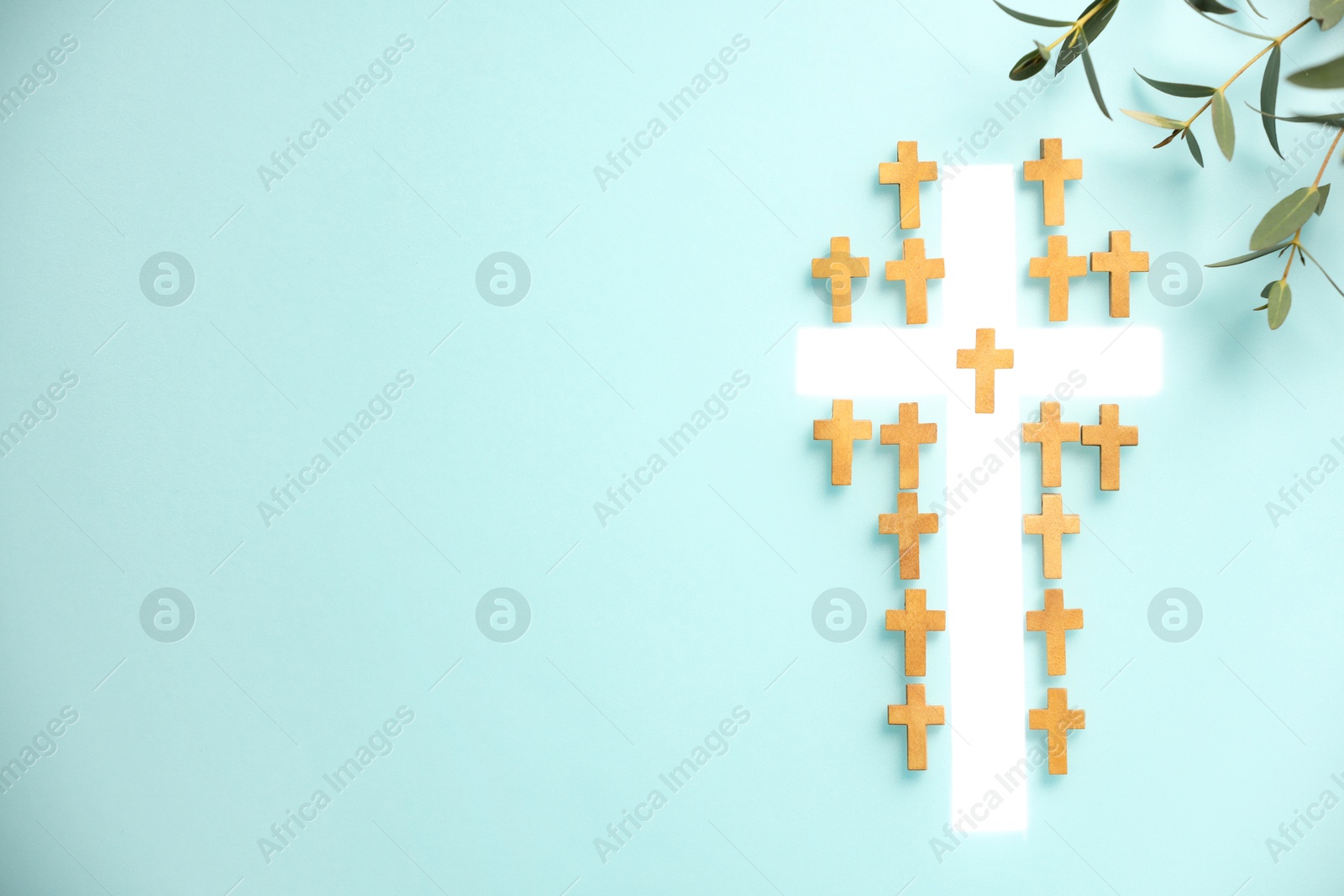 Photo of White cross among small ones and eucalyptus branches on turquoise background, flat lay with space for text. Religion of Christianity