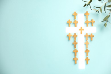 Photo of White cross among small ones and eucalyptus branches on turquoise background, flat lay with space for text. Religion of Christianity