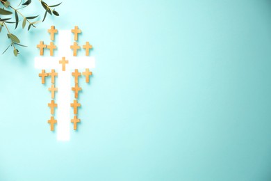 Photo of White cross among small ones and eucalyptus branches on turquoise background, flat lay with space for text. Religion of Christianity