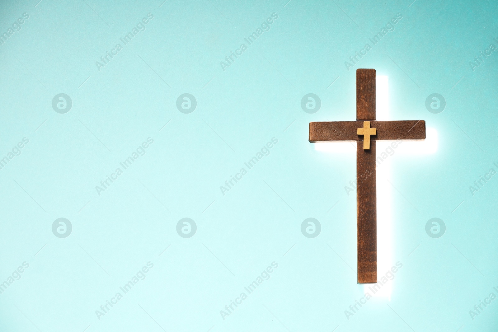 Photo of Shining cross on turquoise background, space for text. Religion of Christianity