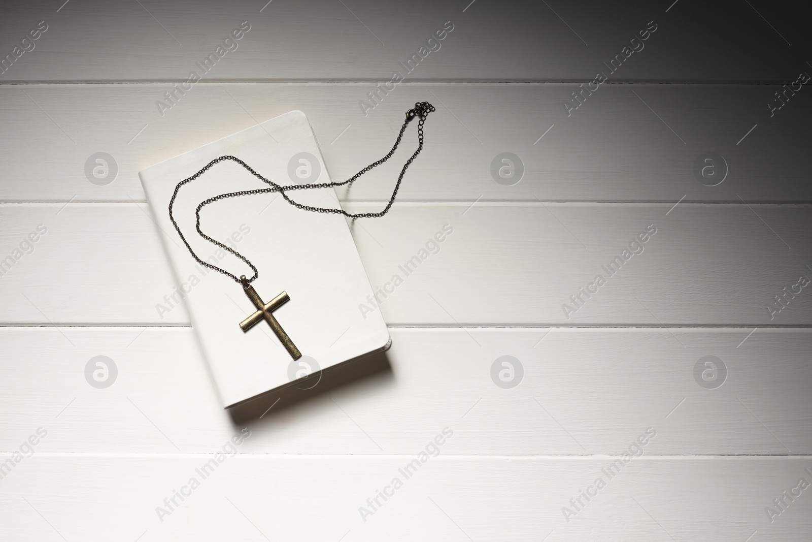 Photo of Cross with chain and Bible on white wooden table, top view with space for text. Religion of Christianity