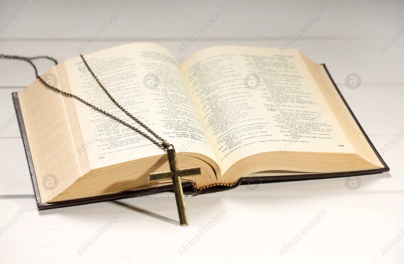 Photo of Cross with chain and Bible on white wooden table, closeup. Religion of Christianity