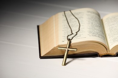 Cross with chain and Bible on white wooden table, closeup with space for text. Religion of Christianity