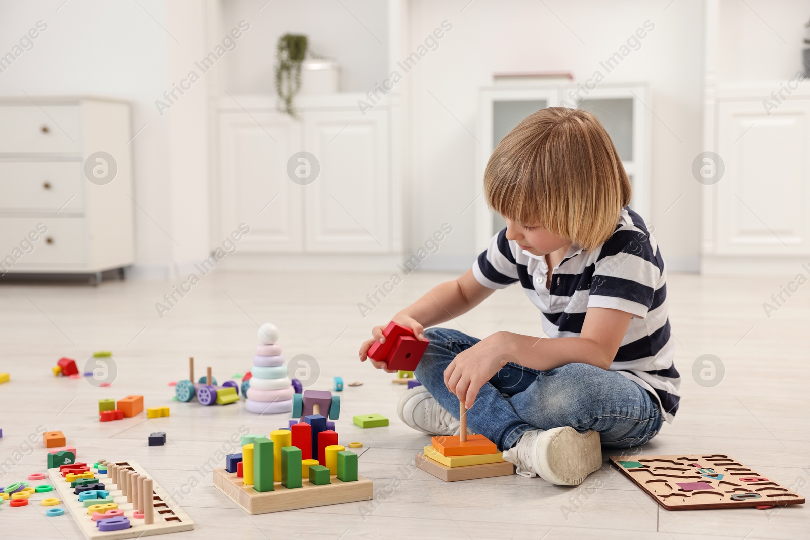 Photo of Cute little boy playing with toy pyramid on floor indoors