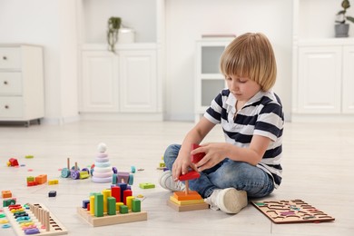 Cute little boy playing with toy pyramid on floor indoors