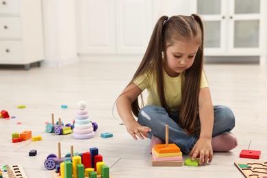 Photo of Cute little girl playing with toy pyramid on floor indoors