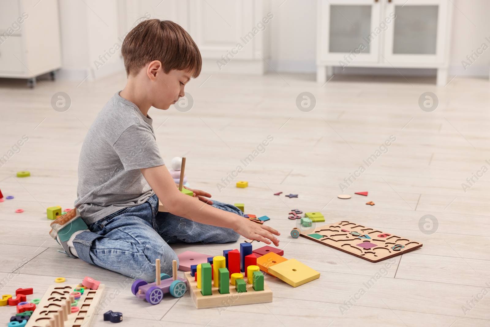 Photo of Cute little boy playing with toy pyramid on floor indoors