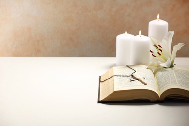 Photo of Cross with chain, burning candles, flower and Bible on white table, space for text. Religion of Christianity