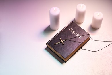 Photo of Cross, burning candles and Bible on table in color lights, above view with space for text. Religion of Christianity