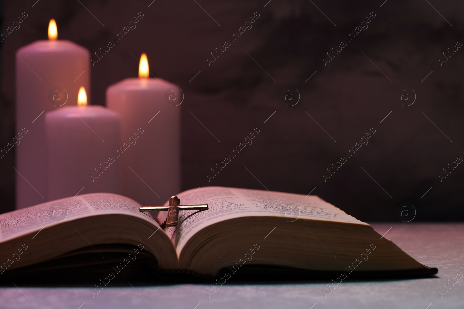 Photo of Cross, Bible and burning candles on textured table against dark background, closeup. Religion of Christianity