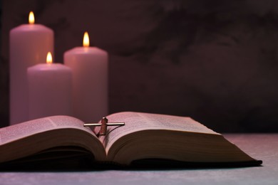 Cross, Bible and burning candles on textured table against dark background, closeup. Religion of Christianity