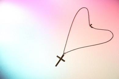 Photo of Cross with chain on textured table in color lights, top view and space for text. Religion of Christianity