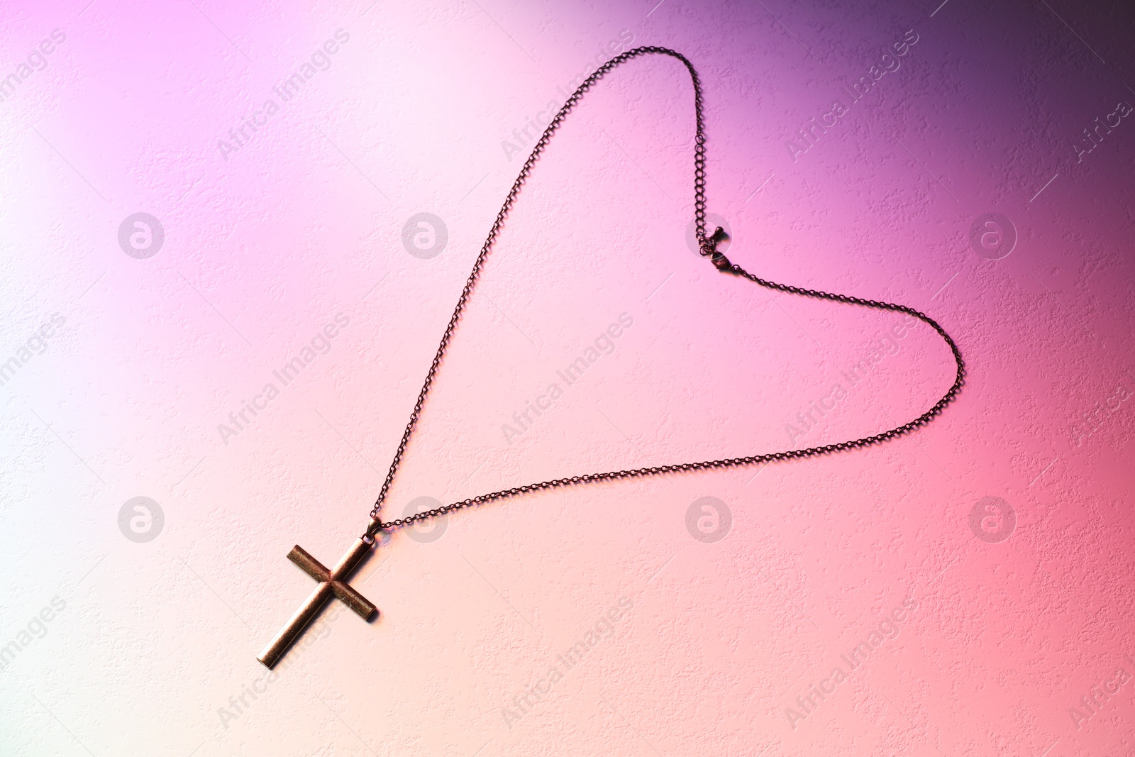 Photo of Cross with chain on textured table in color lights, top view. Religion of Christianity