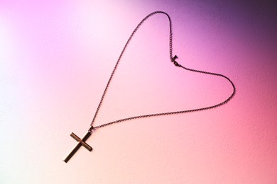 Cross with chain on textured table in color lights, top view. Religion of Christianity