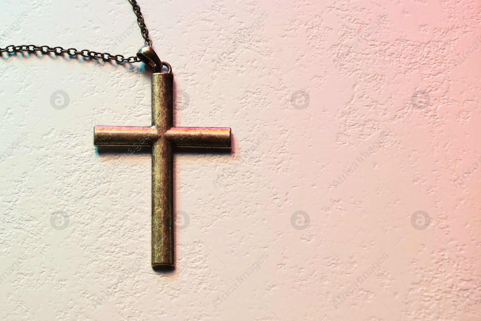 Photo of Cross with chain on textured table in color lights, top view and space for text. Religion of Christianity