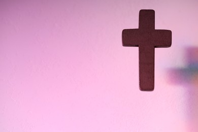 Wooden cross on pink textured background, space for text. Religion of Christianity