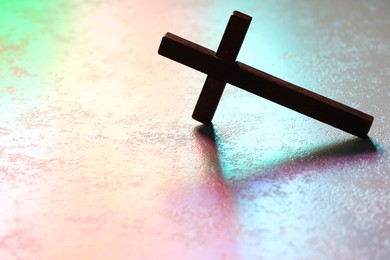 Photo of Wooden cross on textured table in color lights, space for text. Religion of Christianity