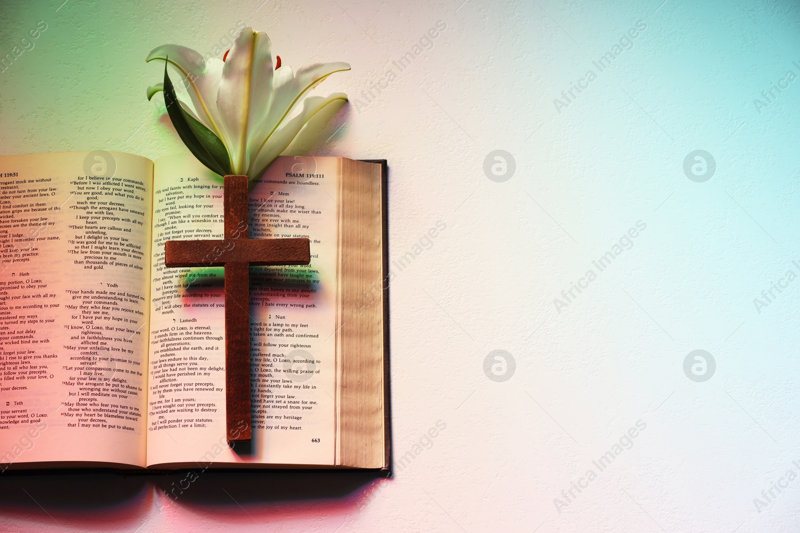 Photo of Wooden cross, Bible and lily flower on textured table in color lights, top view with space for text. Religion of Christianity