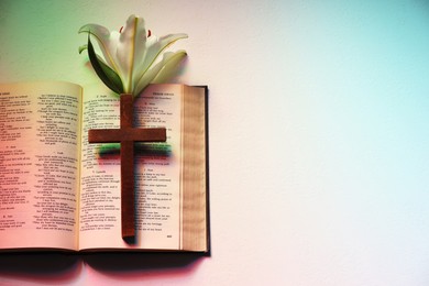 Wooden cross, Bible and lily flower on textured table in color lights, top view with space for text. Religion of Christianity