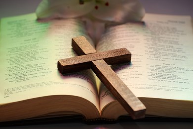 Photo of Wooden cross on Bible in color lights, closeup. Religion of Christianity