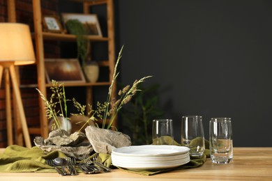 Clean dishes, stones and plants on wooden table in stylish dining room