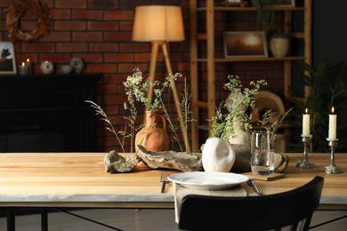 Set of clean dishware, vases with beautiful flowers, stones and burning candles on wooden table in stylish dining room