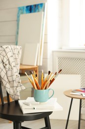 Canvases, paints and cup of brushes on chair in workshop