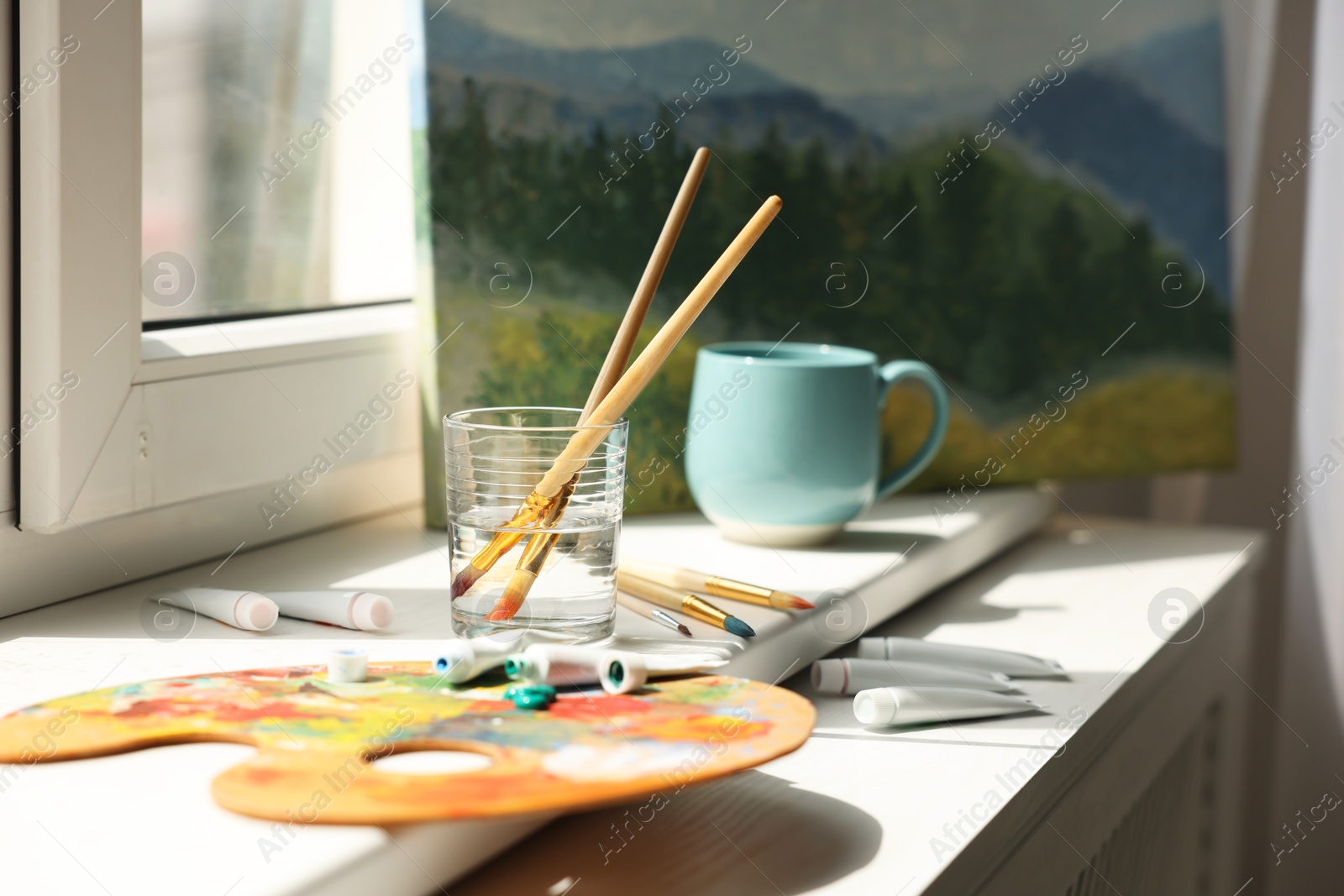 Photo of Artist's palette, brushes in glass of water and paints on window sill