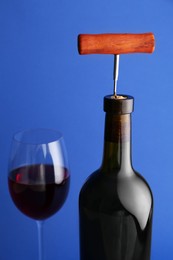 Photo of Bottle with corkscrew and glass of wine on blue background, closeup