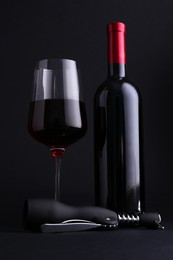 Photo of Wing corkscrew, glass and bottle of red wine on dark background