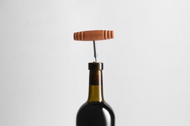 Wine bottle with corkscrew on light grey background