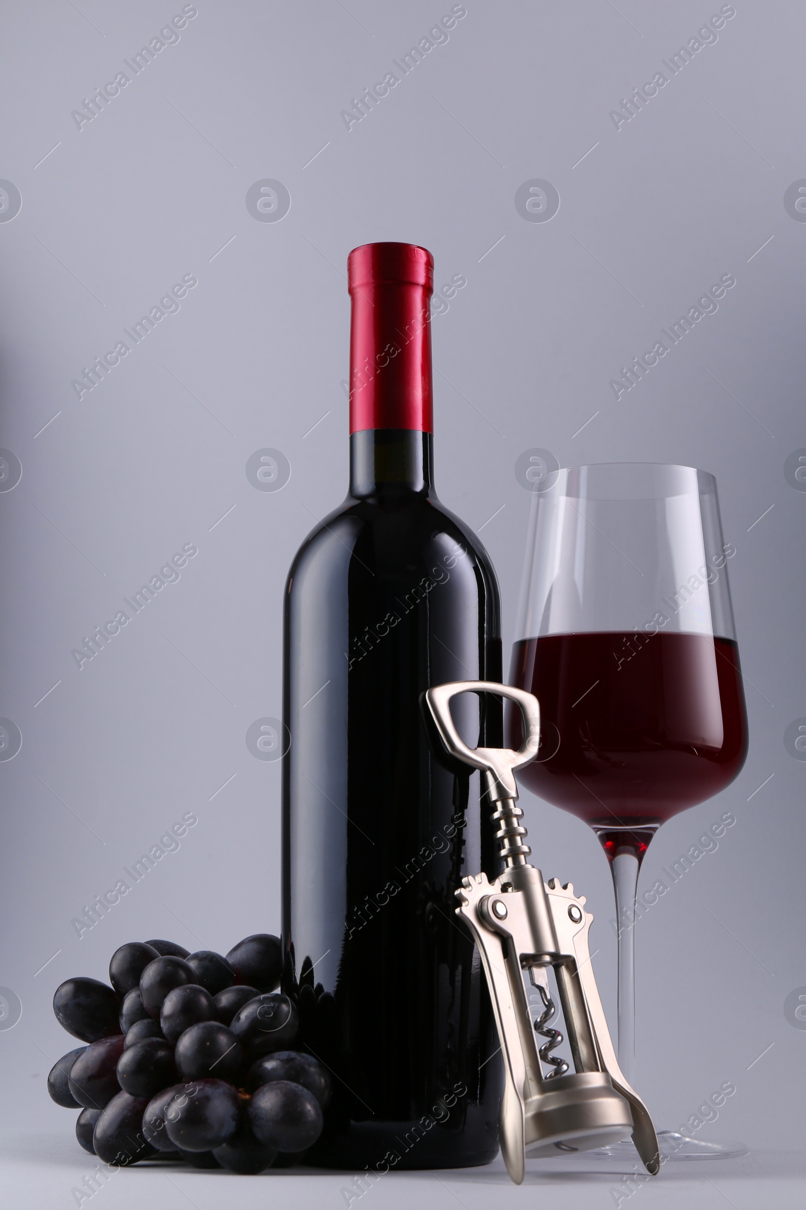 Photo of Red wine, wing corkscrew and fresh grapes on grey background