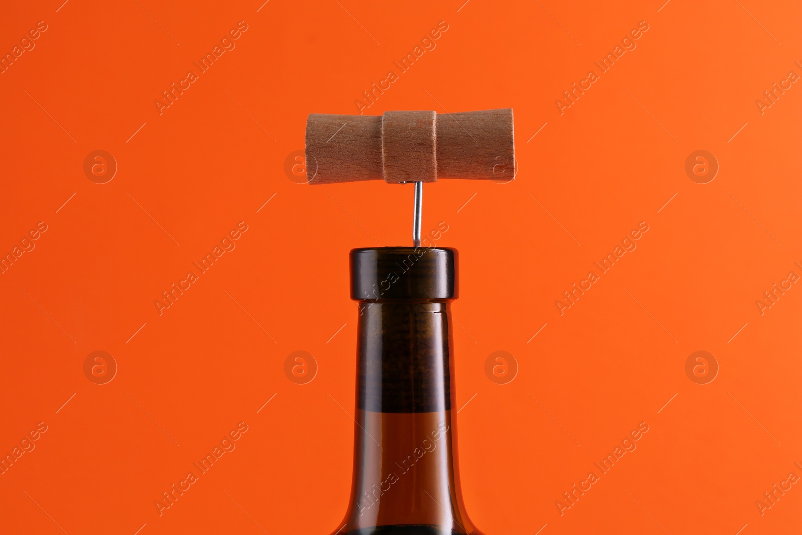 Photo of Wine bottle with corkscrew on orange background, closeup