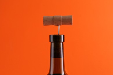 Wine bottle with corkscrew on orange background, closeup