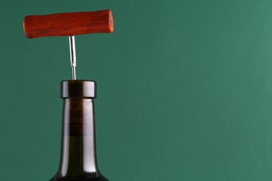 Wine bottle with corkscrew on green background, closeup. Space for text